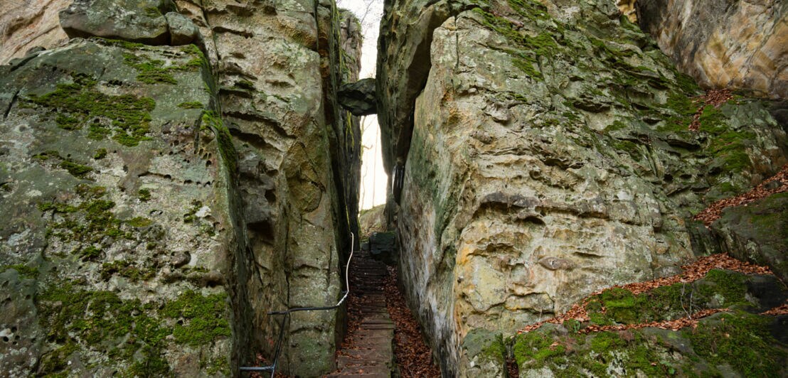 Zwei mächtige Felswände, in deren Mitte eine Spalte ist, in der eine Treppe nach oben führt.