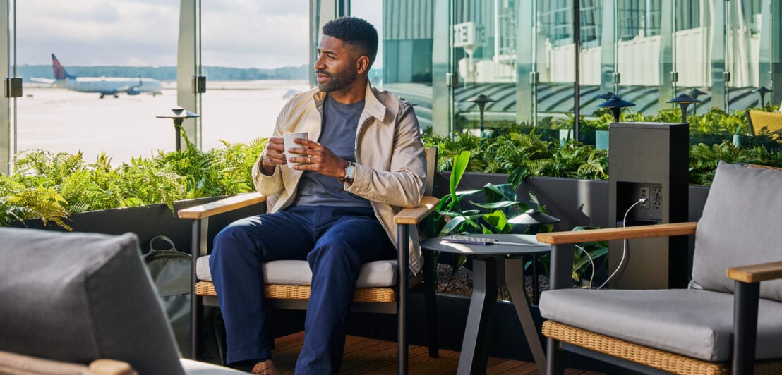 Ein Mann mit Kaffeetasse auf der Terrasse einer modernen Flughafenlounge mit Blick aufs Rollfeld.