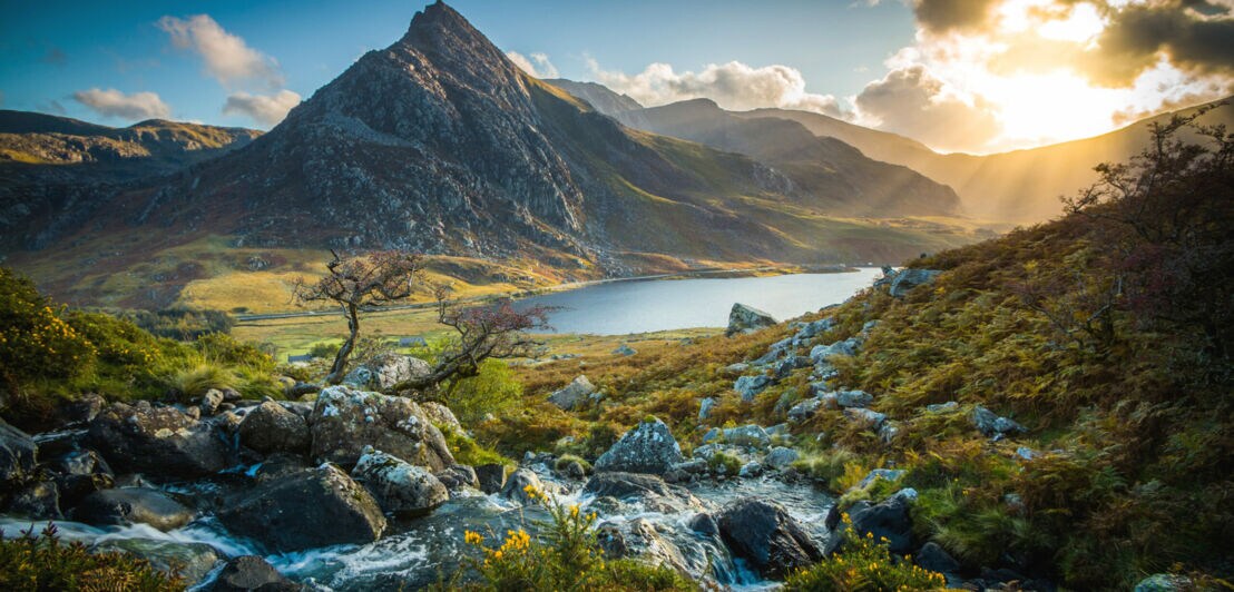 Landschaftspanorama mit Bergsee, umgeben von schroffen Felsen und wilder Natur.