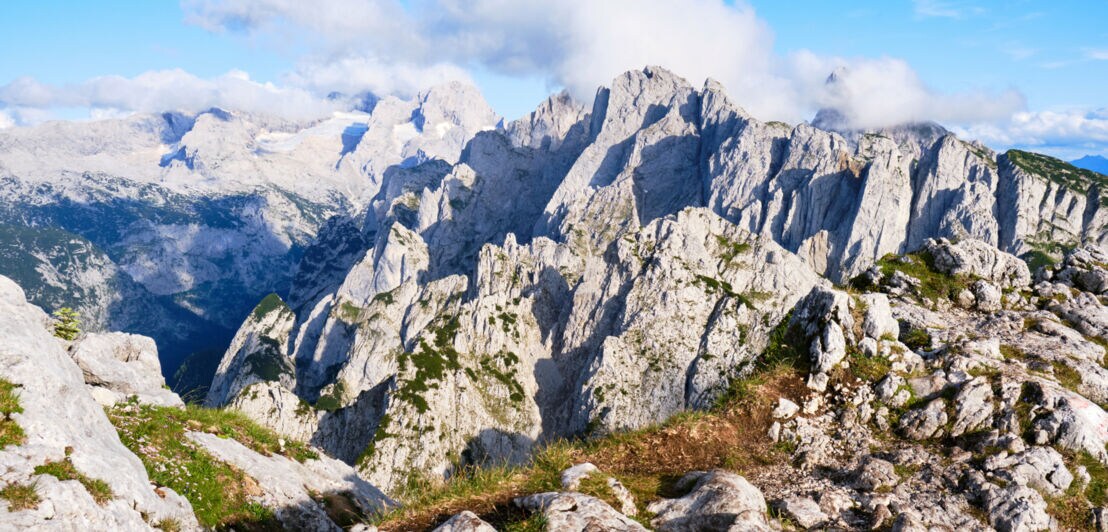 Blick auf teils begrünte Berggipfel und blauen Himmel mit weißen Wolken.