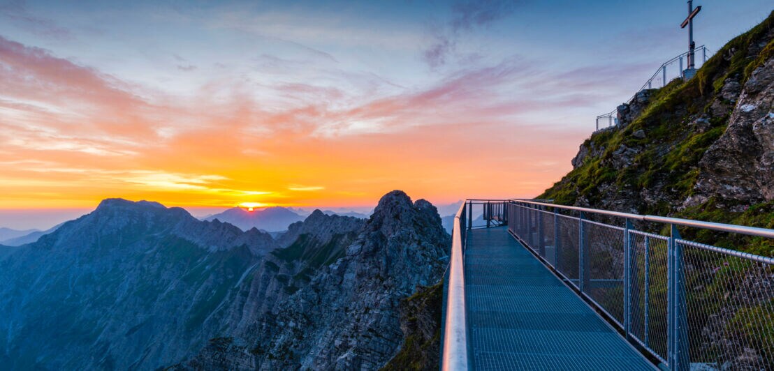 Aussichtsplattform und Gipfelkreuz des Nebelshorns bei Sonnenaufgang.