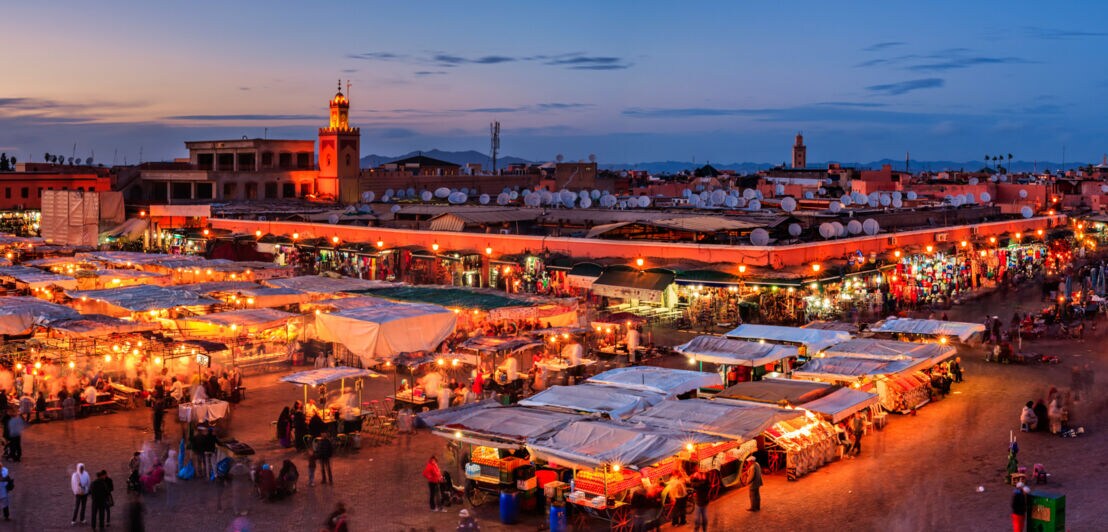 Belebter Marktplatz mit überdachten Ständen im Stadtzentrum von Marrakesch bei Nacht.