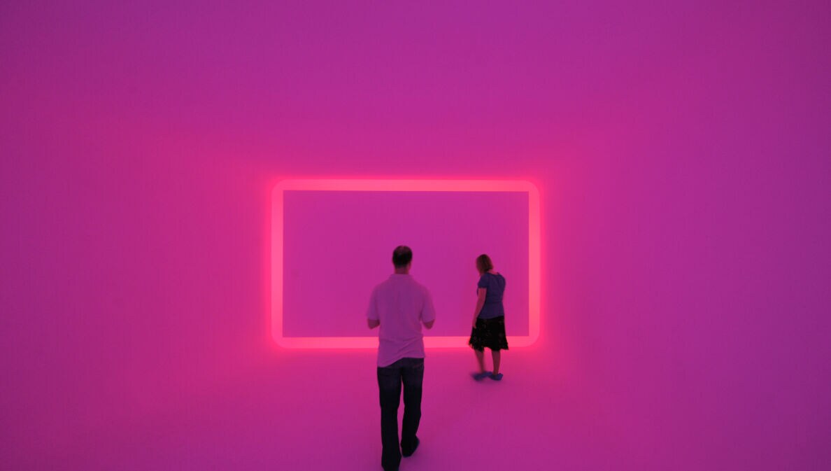 Zwei Museumsbesucher:innen in einem Raum, der pink beleuchtet ist