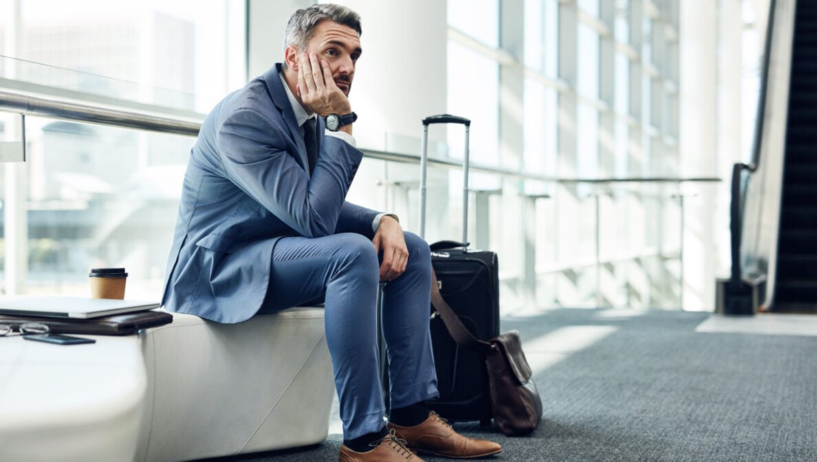 Mann in Anzug auf Sitzmöbel am Flughafen stützt den Kopf in seine Hände