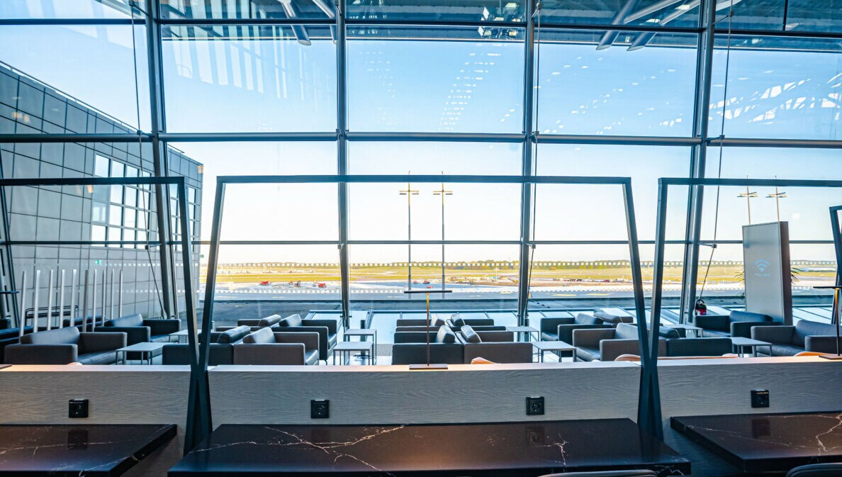 Leere Flughafen-Lounge mit Sitzmöbeln vor Panoramafenstern mit Blick aufs Rollfeld.