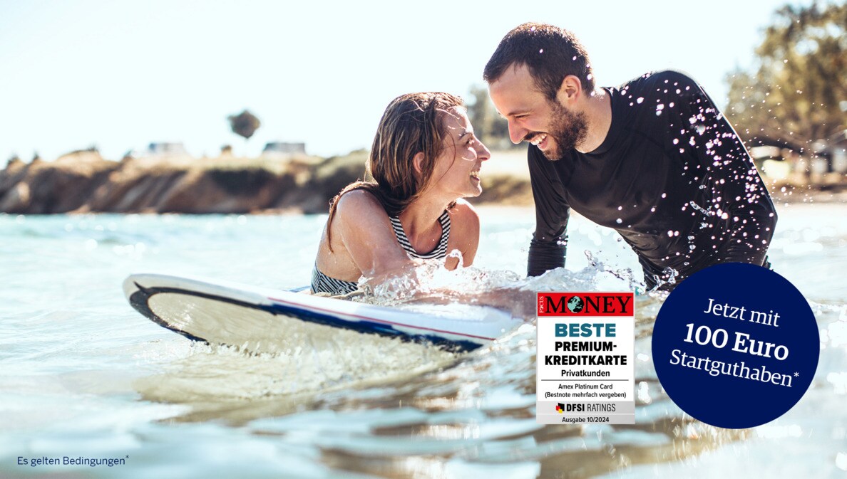 Ein lachendes Paar mit Surfboard im Meer.