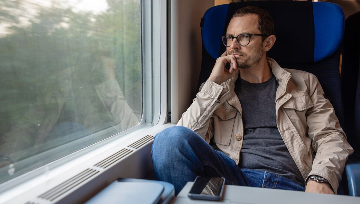 Mann sitzt in fahrendem Zug und schaut aus dem Fenster.