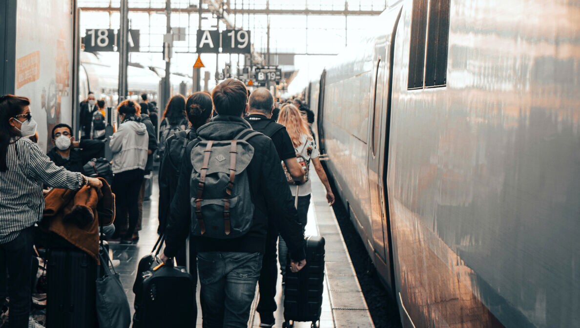 Reisende mit Gepäck laufen am Gleis in einem großen Bahnhof