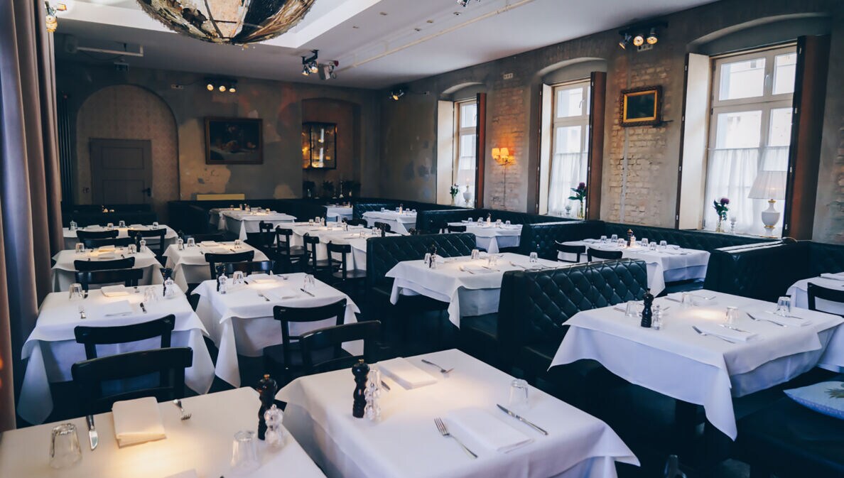 Speisesaal eines trendigen Restaurants mit weiß eingedeckten Tischen und schwarzen Lederbänken.