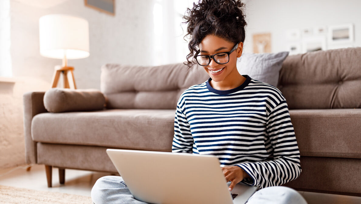 Joyful relaxed ethnic woman using laptop with interest at home