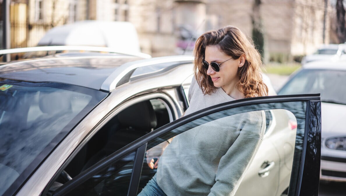 Frau mit Sonnenbrille steigt in parkenden PKW ein