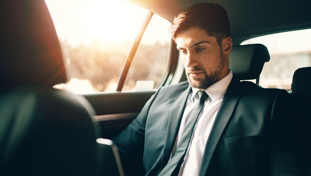 Handsome businessman using laptop while sitting on back seat of a car. Caucasian male business executive travelling by a car and working on laptop computer.