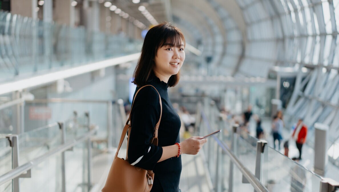 Eine lächelnde asiatische Frau steht in einem Flughafenterminal mit abgerundeter Fassade.