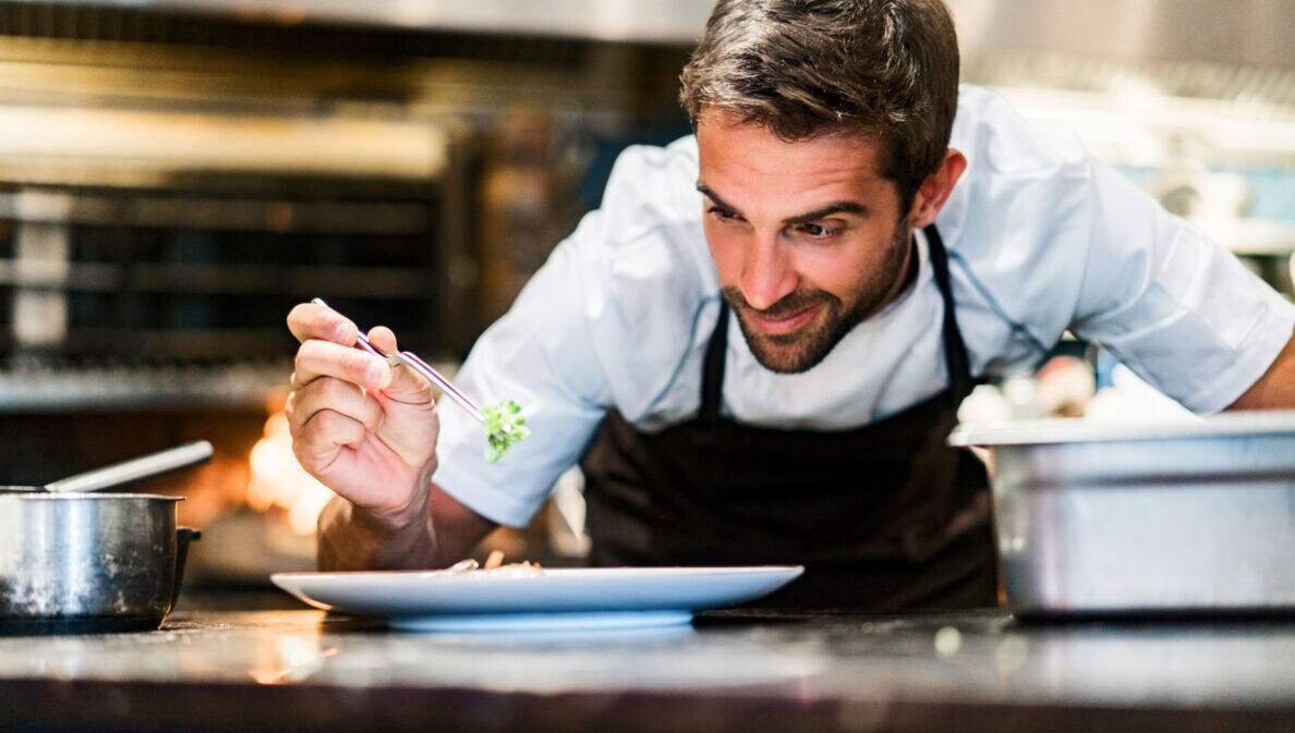 Ein Mann garniert ein Gericht auf einem weißen Teller in einer Restaurantküche.