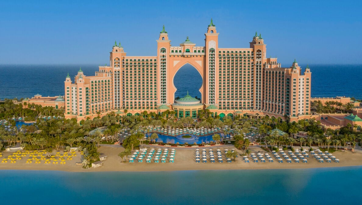 Großer Hotelkomplex im arabischen Stil auf einer Landzunge mit Sandstrand, umgeben von blauem Wasser.