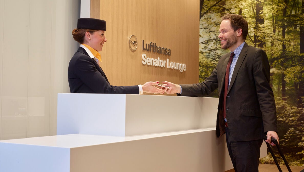 Eine Bodenstewardess begrüßt einen Gast beim Check-in am Empfang einer Lufthansa Senator Flughafenlounge.