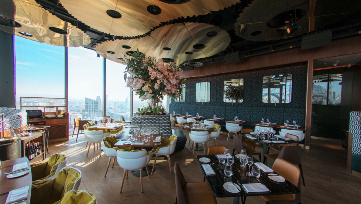 Ein stilvolles Restaurant mit modernen Designelementen und Ausblick auf eine Skyline durch bodentiefe Panoramafenster.