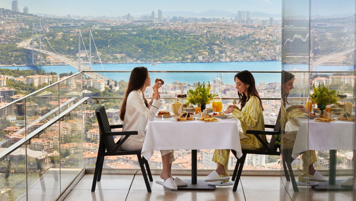 Zwei Frauen frühstücken an einem Tisch auf einem Balkon mit Aussicht auf Istanbul.