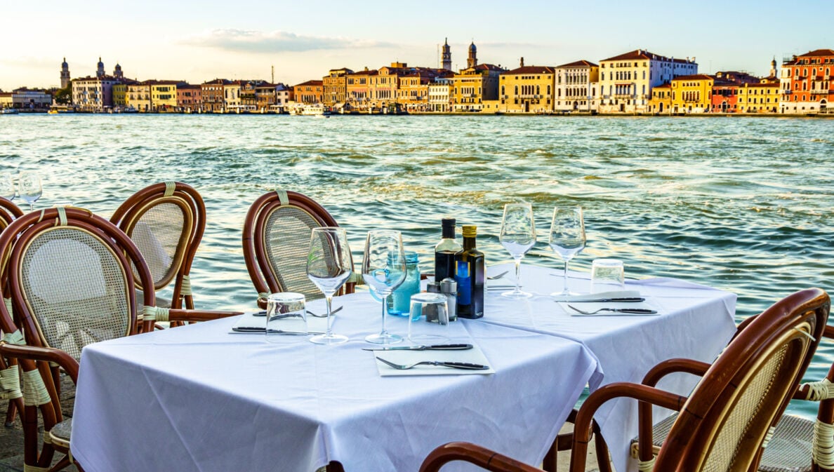 Ein gedeckter Tisch im Außenbereich eines Restaurants am Wasser in Venedig.