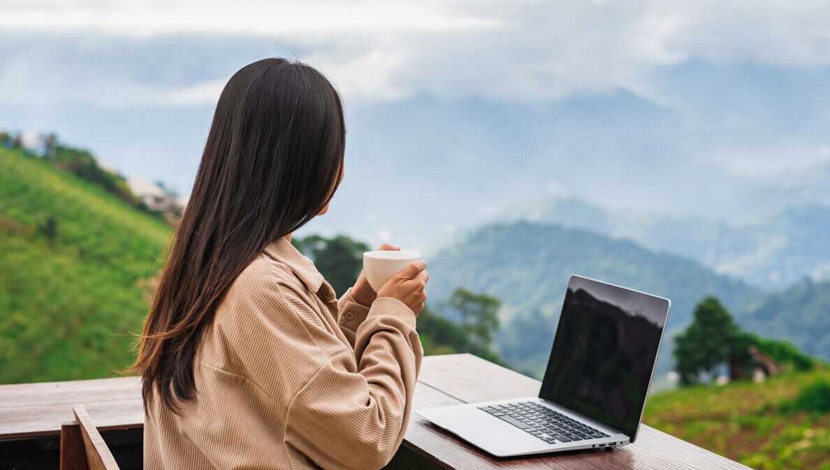Junge Frau arbeitet auf dem Balkon am Laptop und genießt die Aussicht
