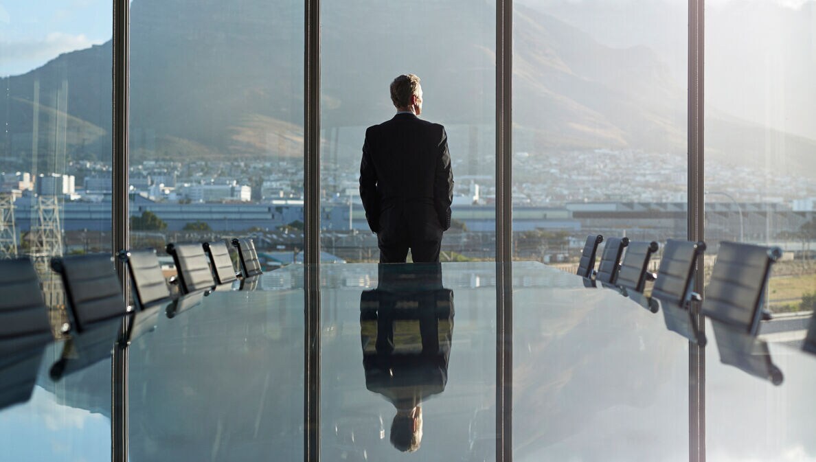 Geschäftsmann blickt aus dem Fenster eines großen Besprechungsraumes auf eine Stadt
