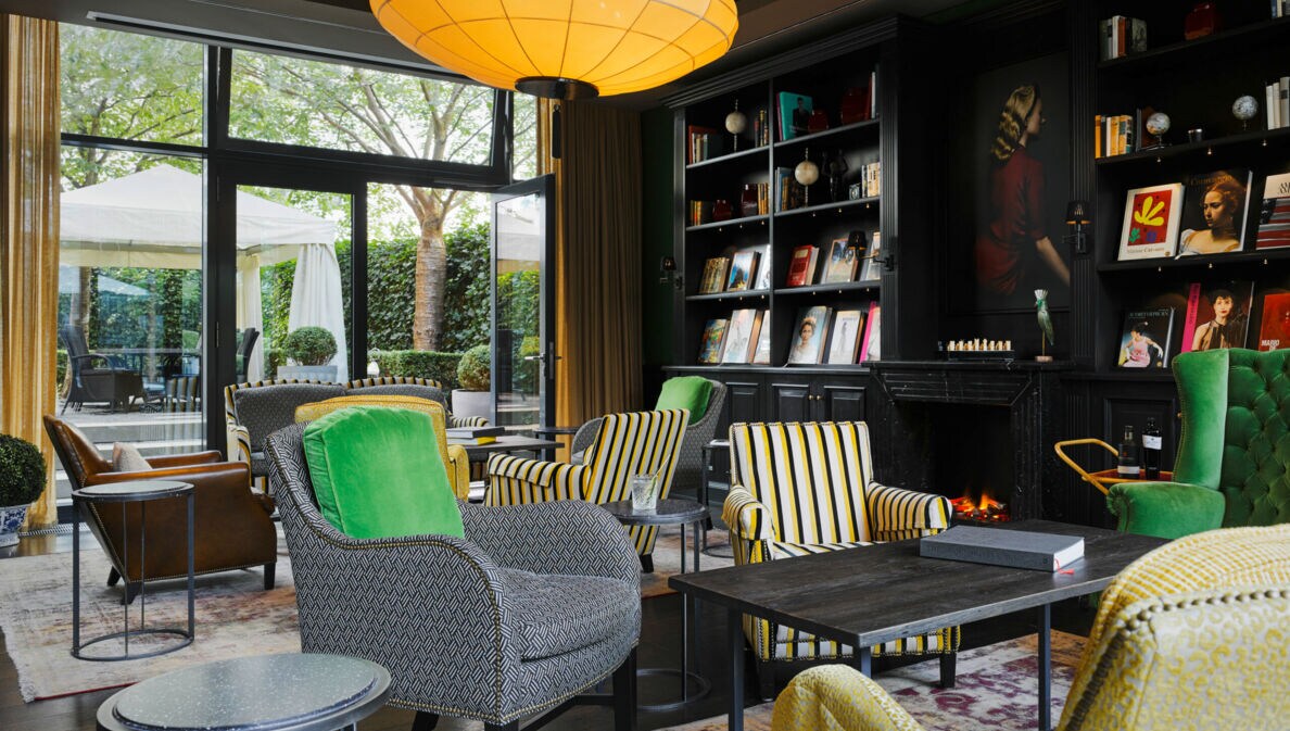 Eine gemütlich eingerichtete Hotellobby mit dunkler Schrankwand, Sesseln in Grau- und Gelbtönen und einer großen Glasfront mit Blick auf die Terrasse