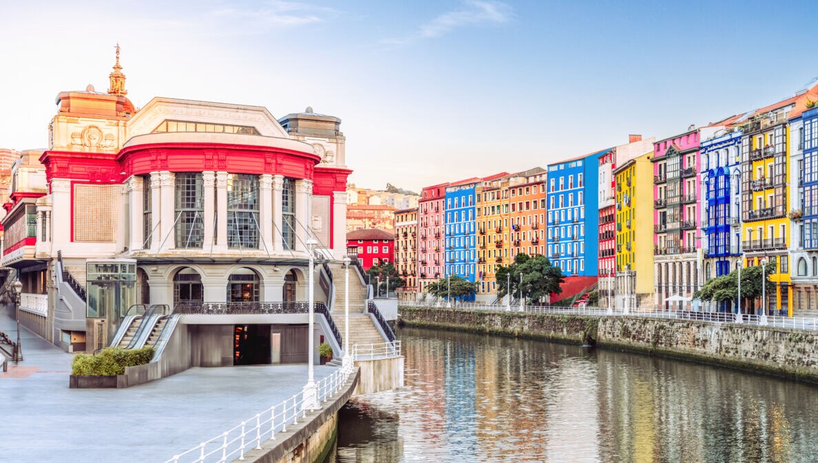 Der Mercado de la Ribera in Bilbao am linken Ufer eines Flusses, auf der anderen Flussseite befinden sich weitere bunte Häuser.