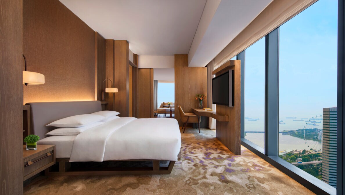 Moderne Hotelsuite mit Holzelementen und Aussicht auf das Hafengebiet von Singapur durch raumhohe Panoramafenster.