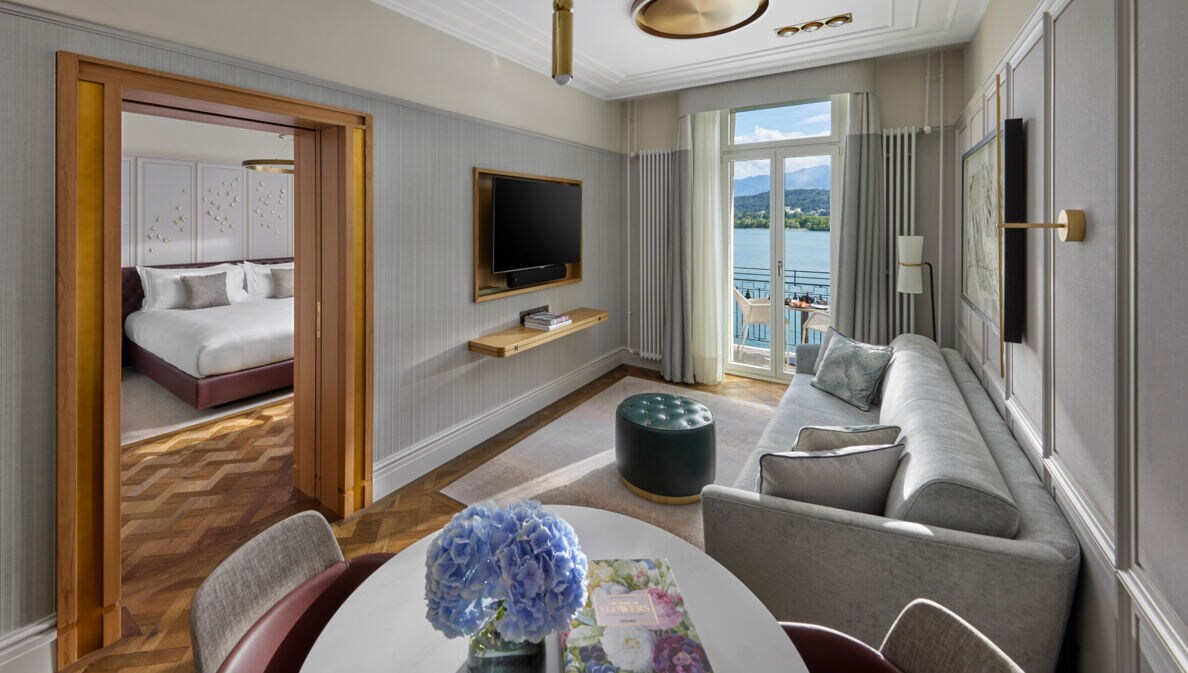 Elegante Hotelsuite mit Balkon an einem See vor Bergpanorama.