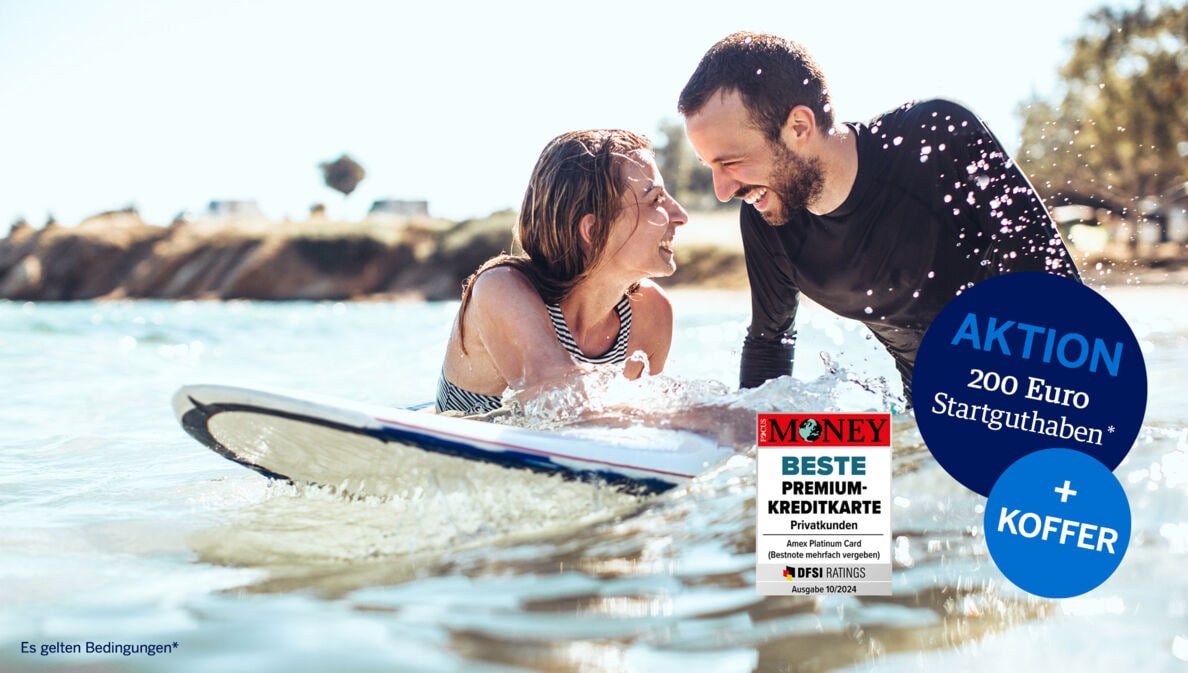 Ein lachendes Paar mit Surfboard im Meer.