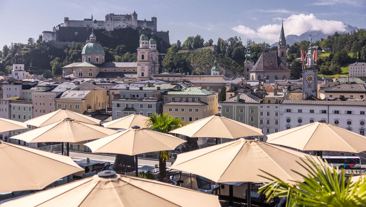 Panorama der Salzburger Altstadt mit Burg auf einem Berg am Fluss, im Hotelterrasse mit Sonnenschirmen.