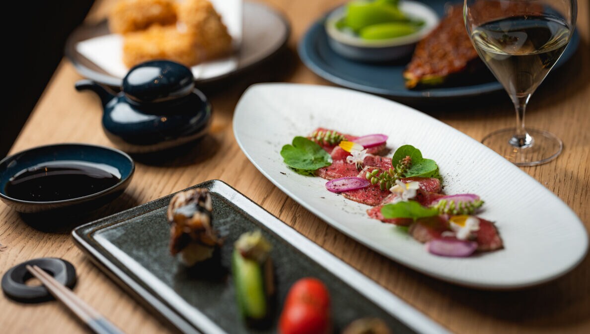 Gedeckter Holztisch mit japanischen Tapas und Sushi-Kreationen.