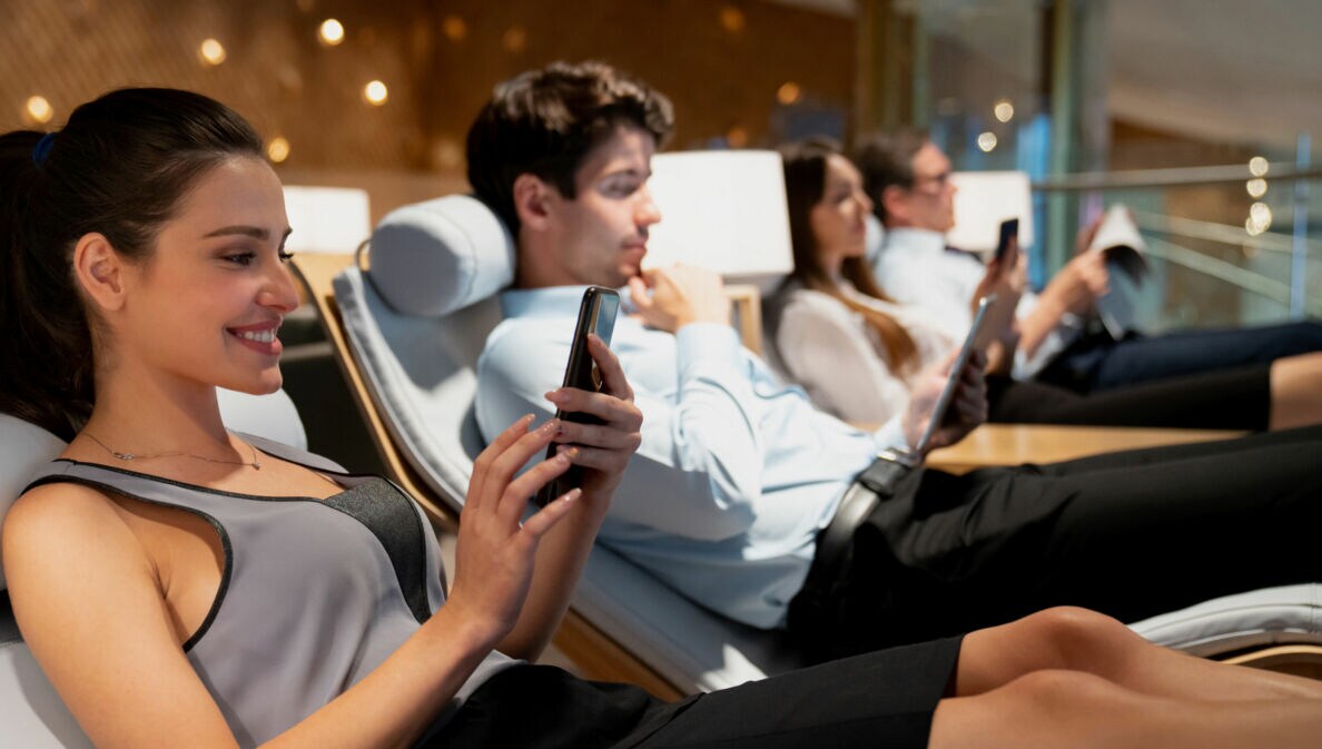 Vier Personen nebeneinander auf Liegen in einer Flughafen-Lounge.