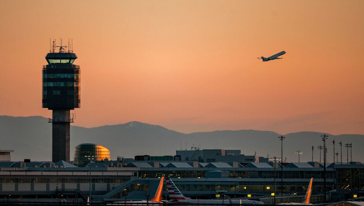 Tower des Vancouver Airports bei Sonnenuntergang und ein startendes Flugzeug.