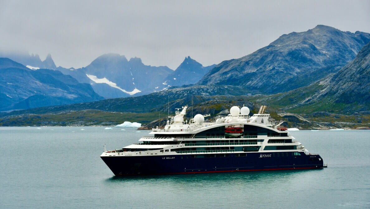 Das Bild zeigt im Vordergrund das Kreuzfahrtschiff. Im Hintergrund sind Berge und etwas Schnee und Eis zu sehen.