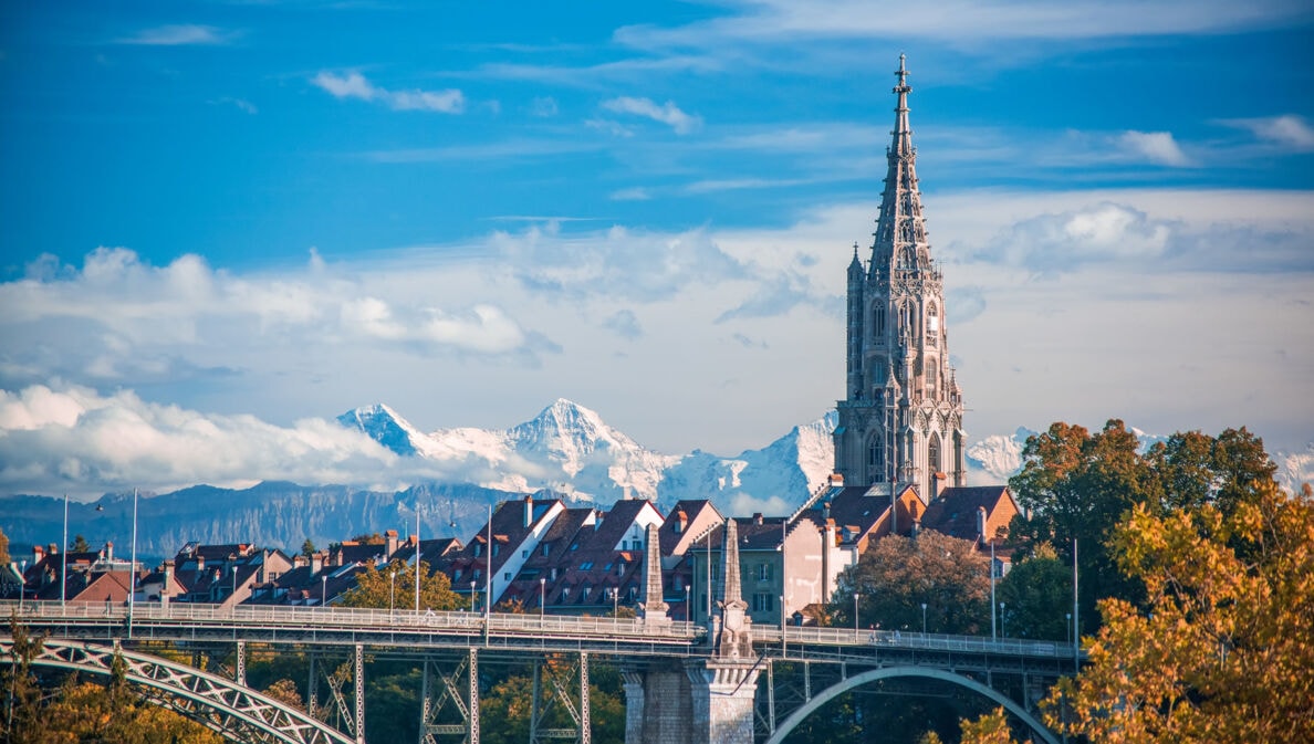 Turm der Kathedrale von Bern mit schneebedeckten Gipfeln im Hintergrund.