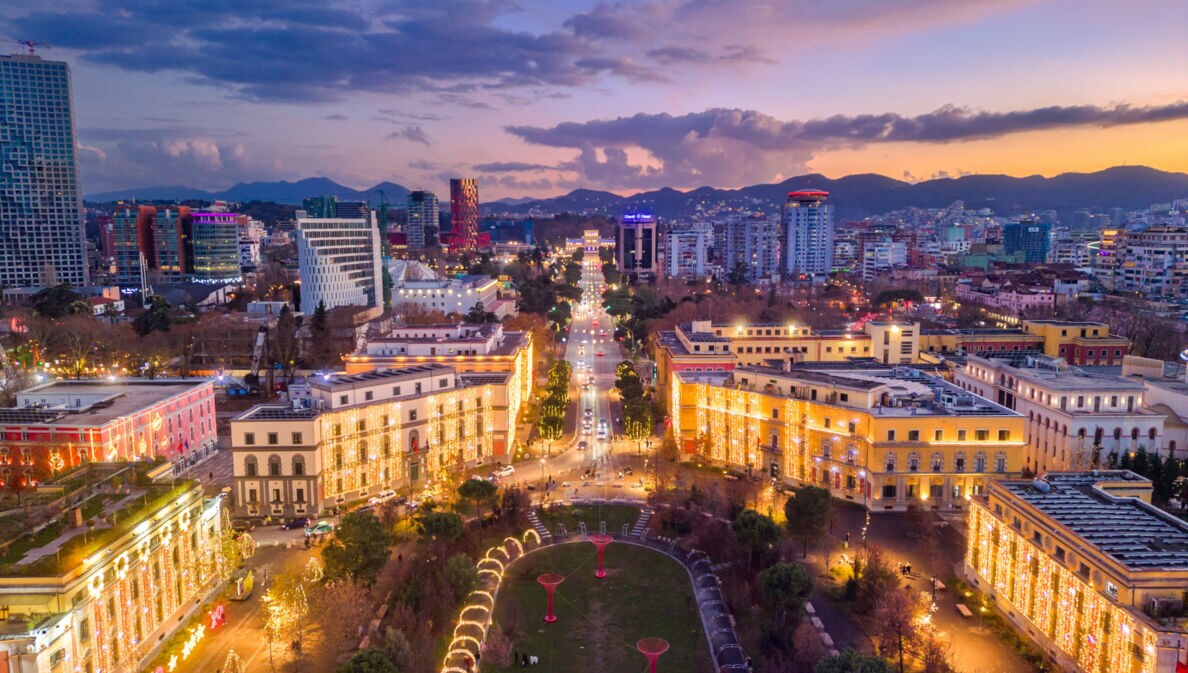 Beleuchtetes Stadtpanorama von Tirana bei Abenddämmerung aus der Luftperspektive.