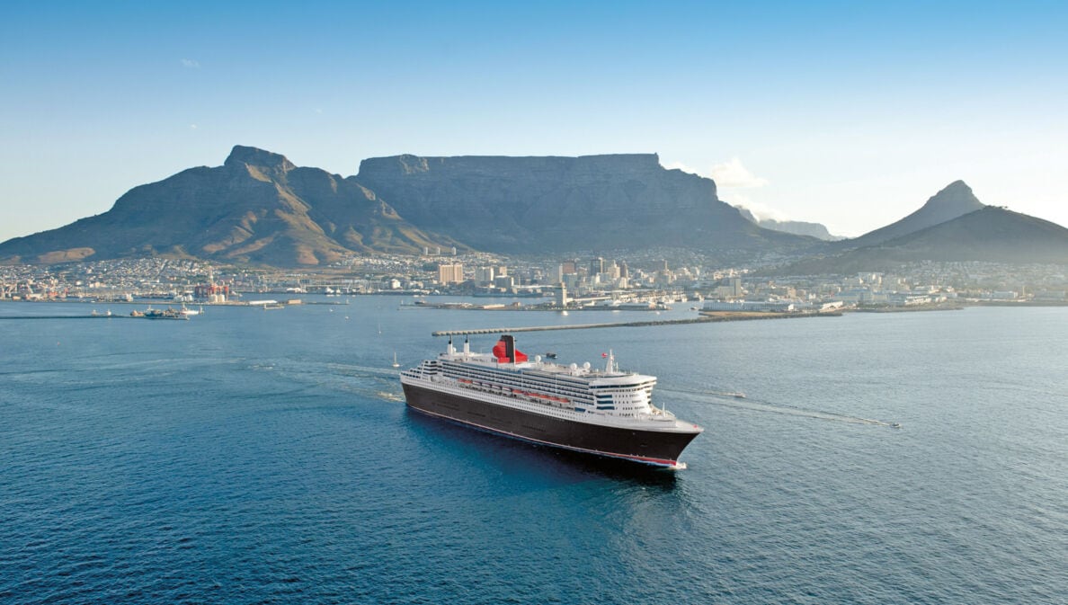 Kreuzfahrtschiff Queen Mary 2 im Wasser vor der Skyline Kapstadts.