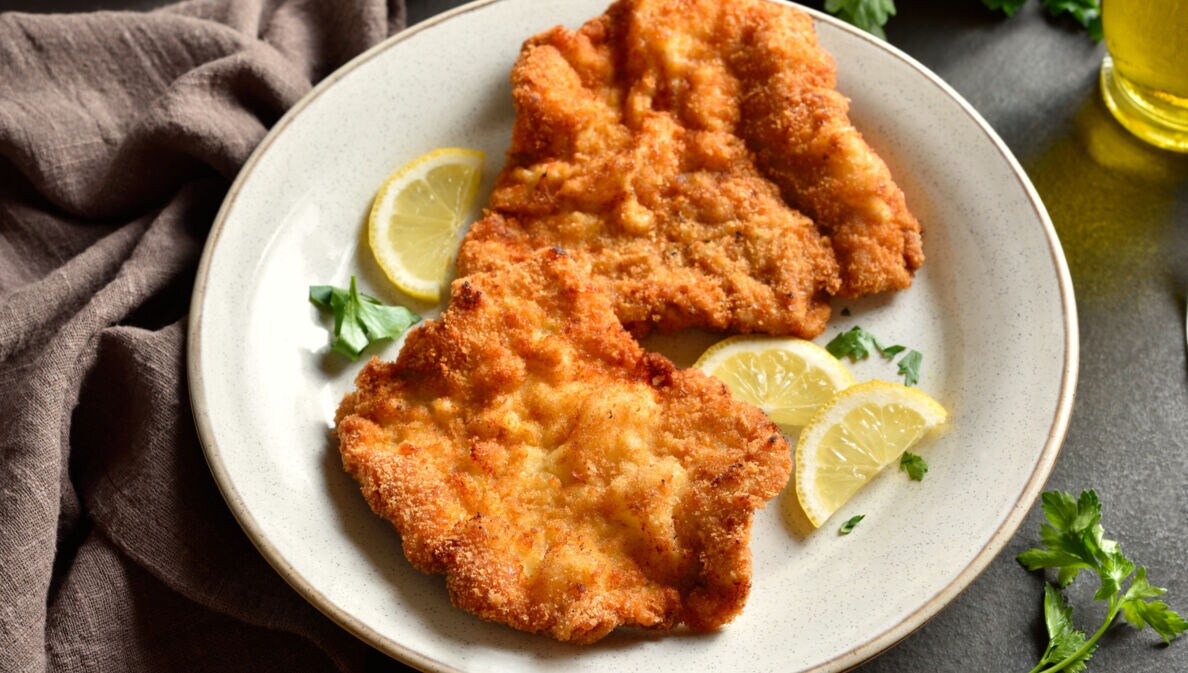 Ein Wiener Schnitzel auf einem Teller mit Zitronenscheiben.