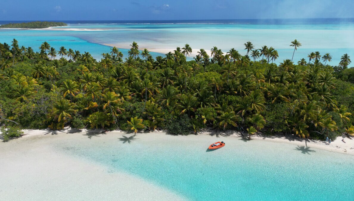 Südseeinsel mit Palmenwald an einer trürkisblauen Lagune mit weißem Sandstrand.