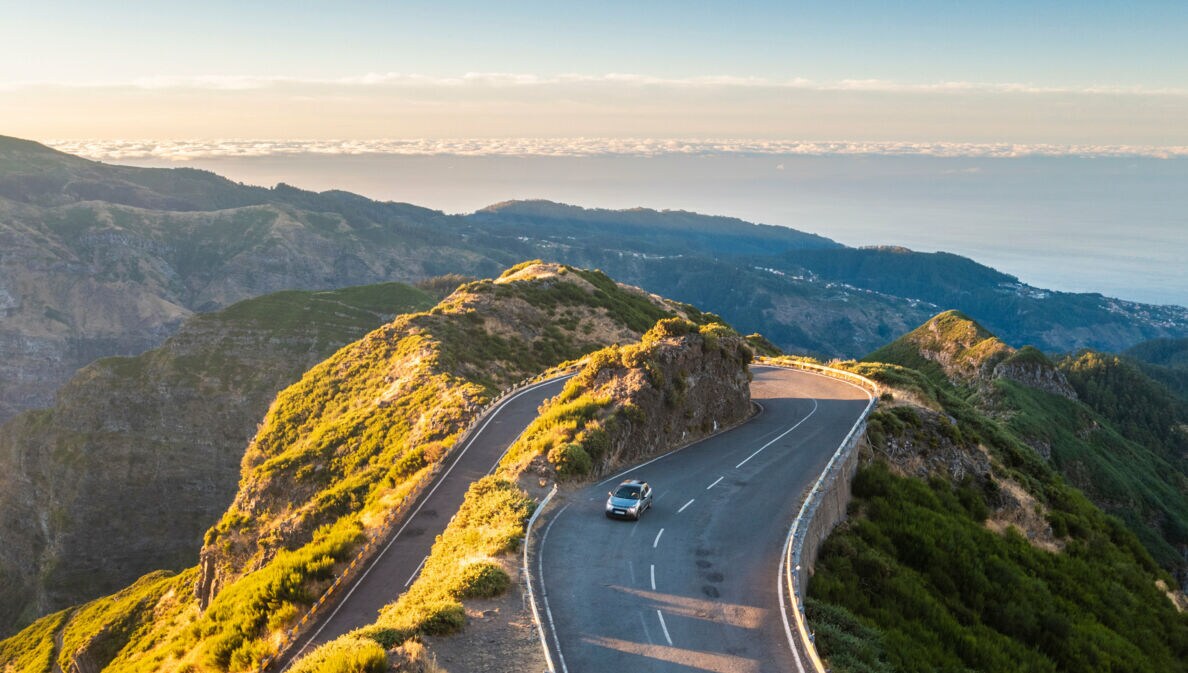 Ein Auto auf einer kurvigen Straße durch eine hügelige Landschaft auf Madeira.