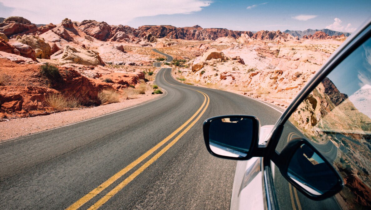 Seitenspiegel eines Autos auf einer US-amerikanischen Autobahn in einer felsigen Wüstenlandschaft.