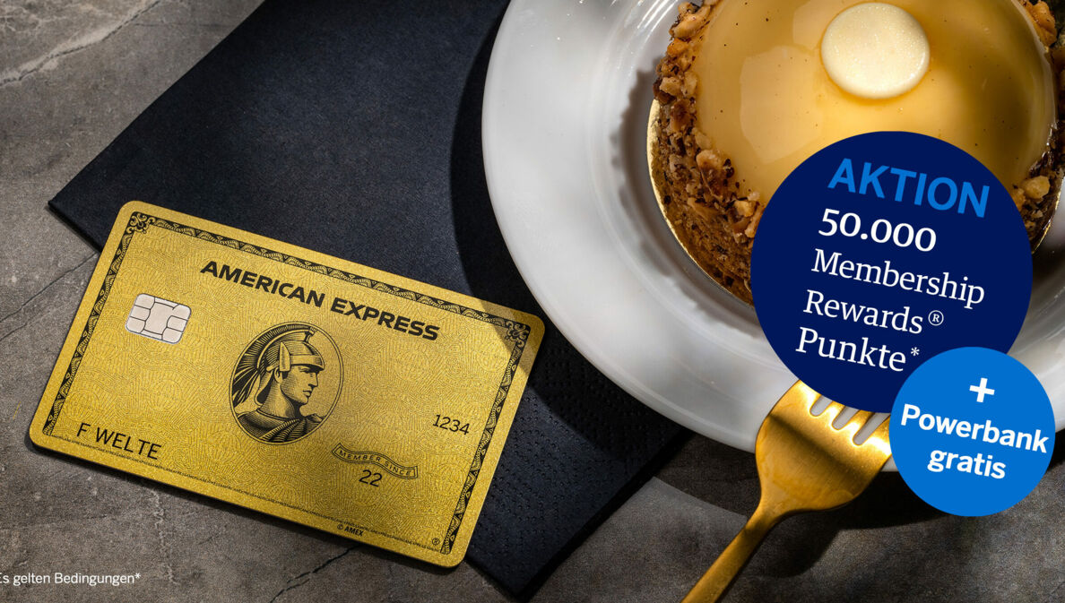 Eine goldene Kreditkarte von American Express liegt auf einer schwarzen Serviette neben einem goldfarbenen Törtchen auf einem Teller und einer goldenen Gabel.