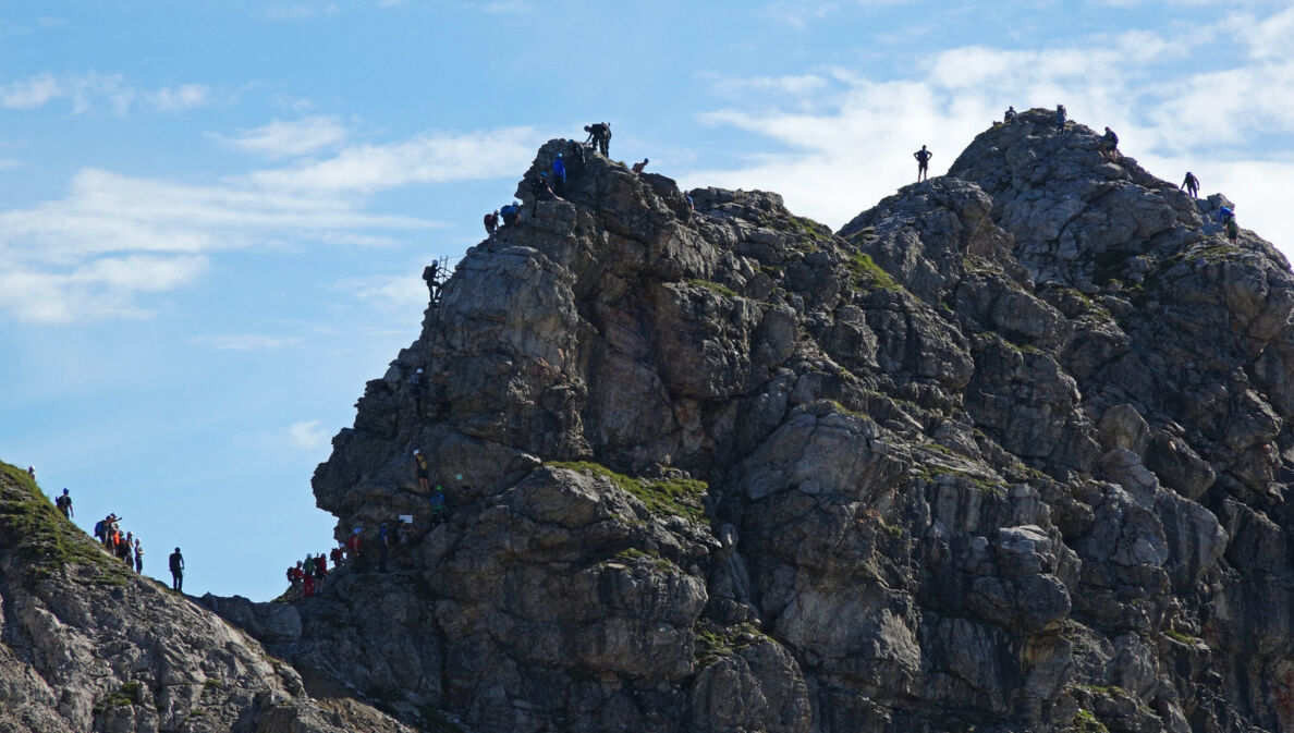 Mehrere Personen, die einen Felsen am Hindelanger Klettersteig erklimmen.