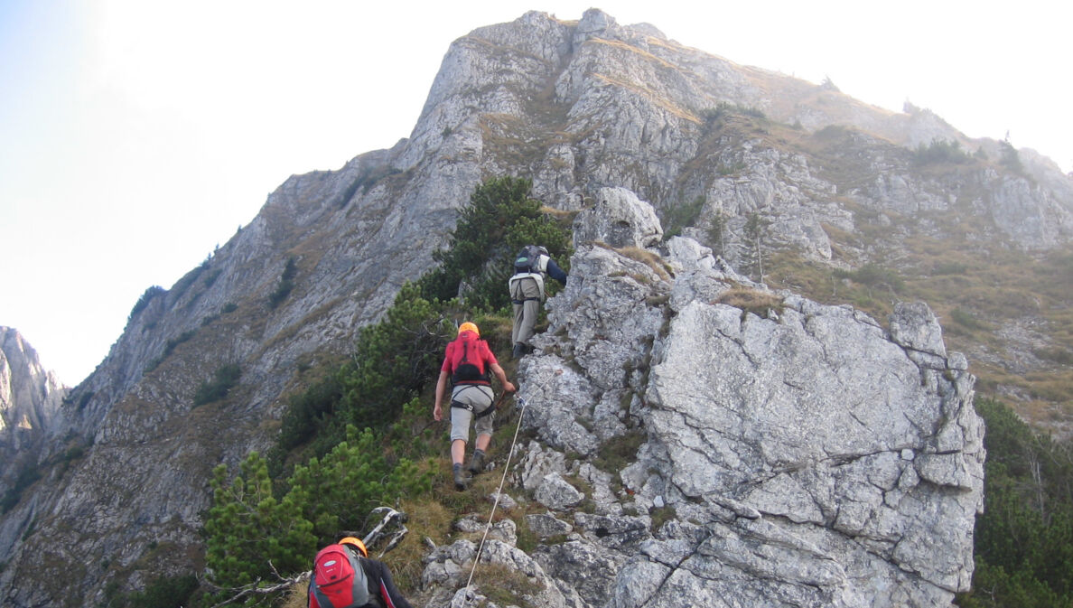 Drei Personen in Kletterausrüstung an einem Felsen an einem der Tegelberger Klettersteige.