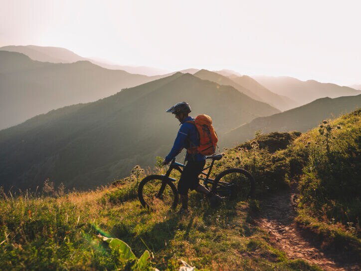 Mountainbiker steht mit seinem Rad auf einem Berg und schaut ins Tal