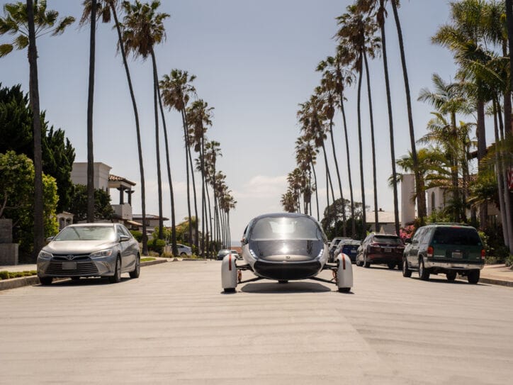 Ein futuristisches Fahrzeug fährt in der Sonne auf palmengesäumter Straße