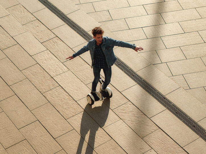 Ein lachender, junger Mann in Jeansjacke auf einem weißen Hoverboard