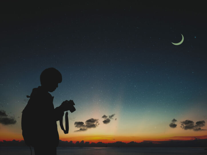 Ein Fotograf sieht in der Dunkelheit auf seine Kamera, am Himmel steht der Mond.