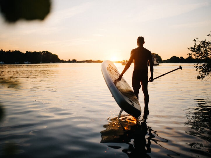 Mann trägt ein SUP Board ins Wasser